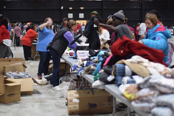 A lot of people in a warehouse type room where some people are volunteering and some are picking up free clothing.